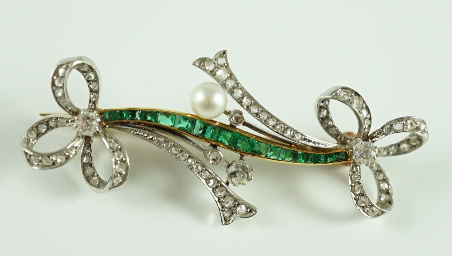 A Belle Epoque gold and platinum, emerald, diamond and seed pearl set twin ribbon bow bar brooch